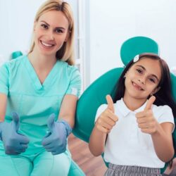 little girl in dental share holding a thumbs up next to her dentist