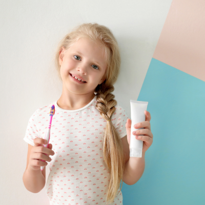 Little girl smiling, holding toothbrush and toothpaste