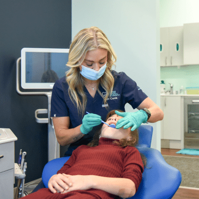 a RPDO dentist in a blue medical uniform and gloves brushing a patient's teeth, representing dental sealants for children