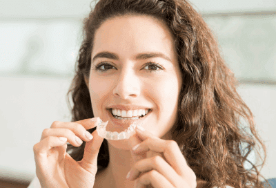 a woman smiling holding clear aligners, representing adult orthodontics in VA