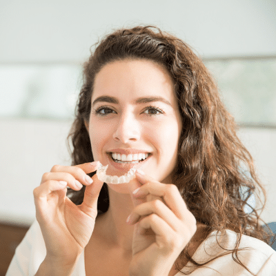 a woman smiling holding clear aligners, representing adult orthodontics in VA