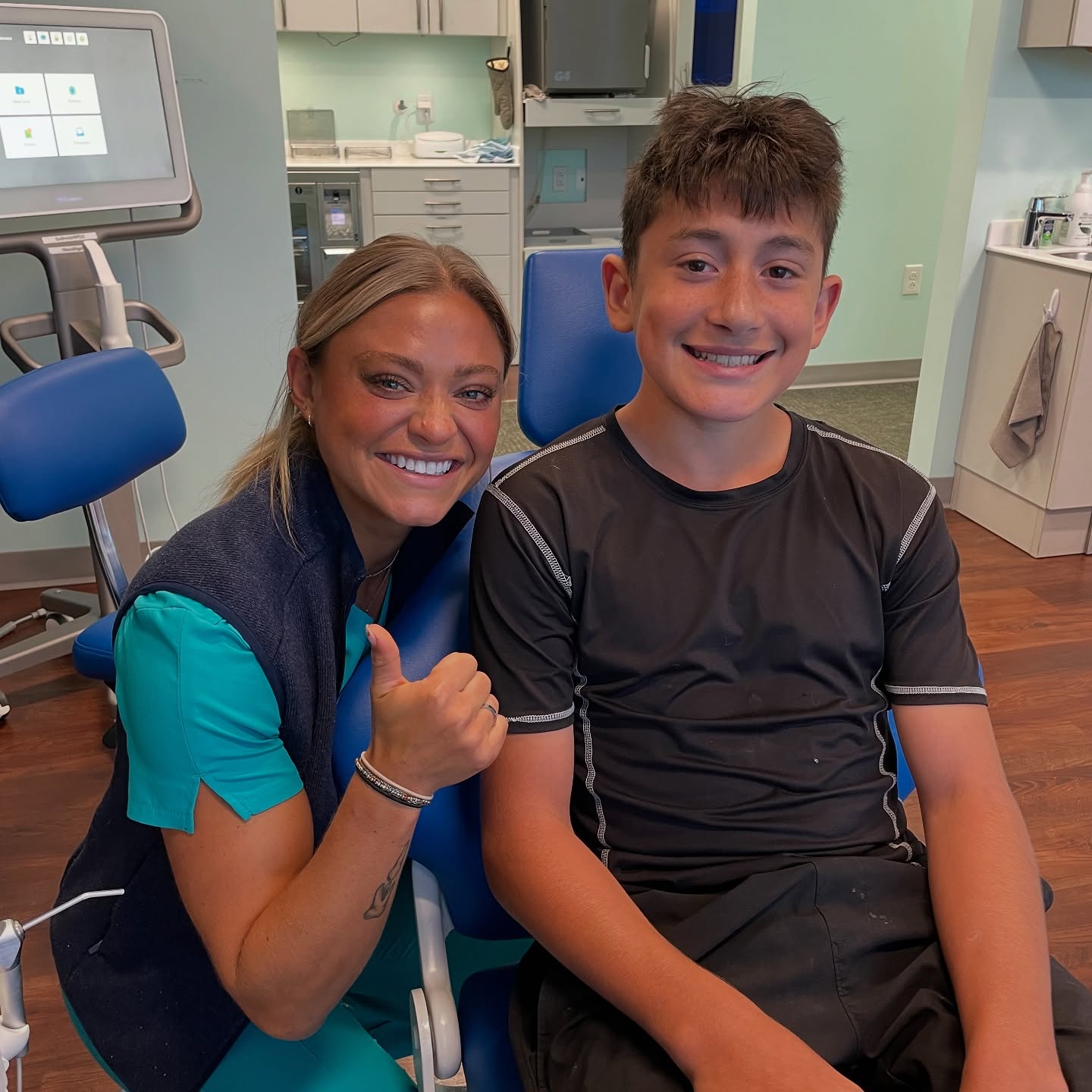 RPDO team member and teen patient smiling after open bite treatment in Richmond, VA — teal-colored operatory at Richmond Pediatric Dentistry and Orthodontics