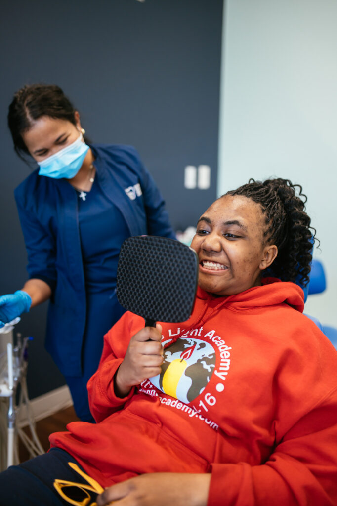 Location Richmond 7 Teen patient smiling at her new smile in a hand mirror on braces-off day at RPDO