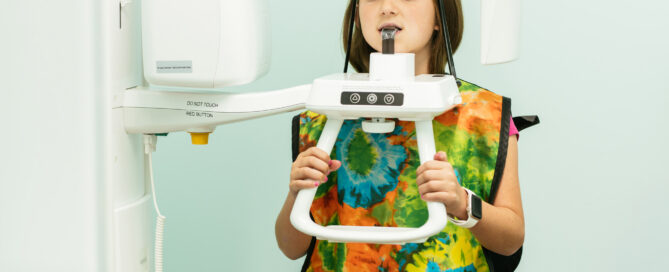 Young patient wearing a colorful lead apron and using a panoramic dental X-ray machine at Richmond Pediatric Dentistry and Orthodontics