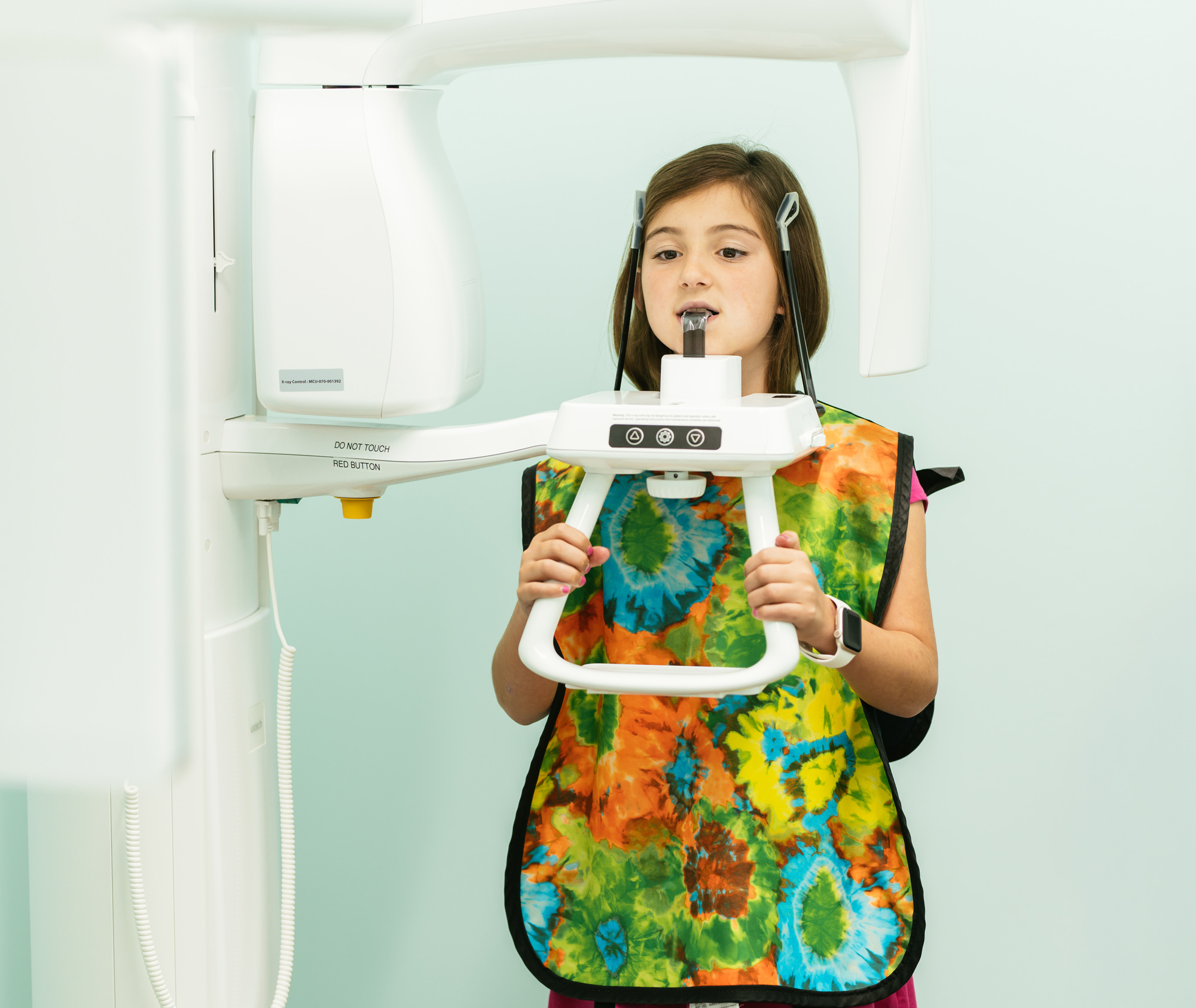 Young patient wearing a colorful lead apron and using a panoramic dental X-ray machine at Richmond Pediatric Dentistry and Orthodontics