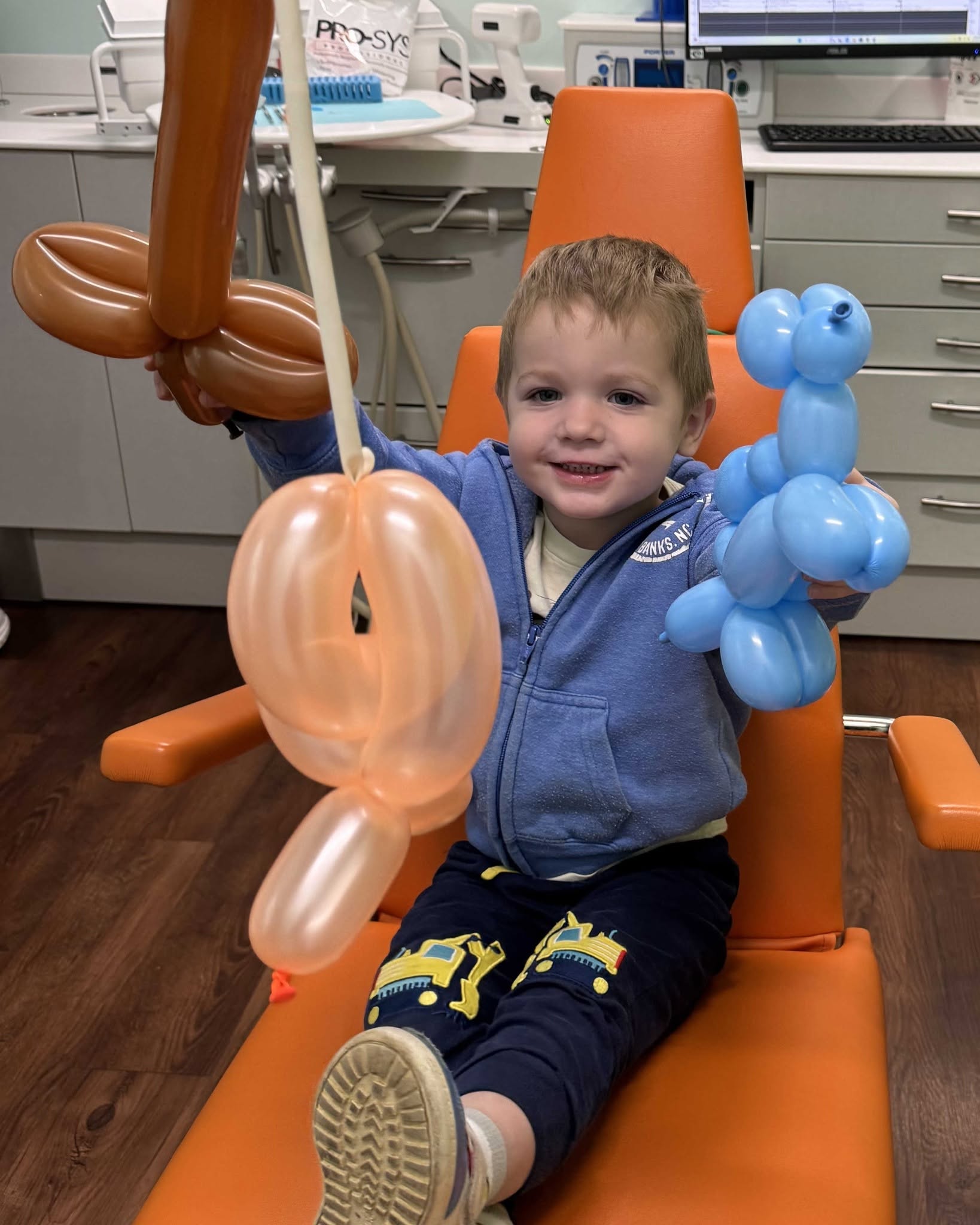 Smiling young child holding balloon animals in the dental chair at RPDO in the Richmond, VA area