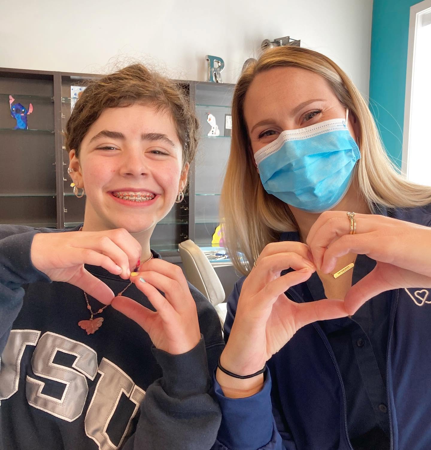 Smiling teen with braces making a heart shape with a team member at Richmond Pediatric Dentistry and Orthodontics