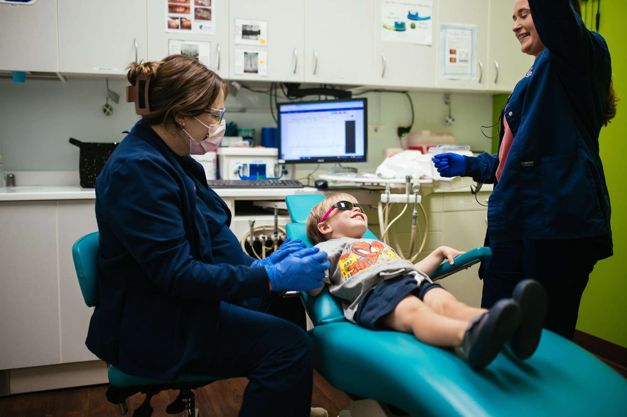 Pediatric dentist and assistant talking with a relaxed young boy wearing sunglasses in the dental chair at Richmond Pediatric Dentistry and Orthodontics