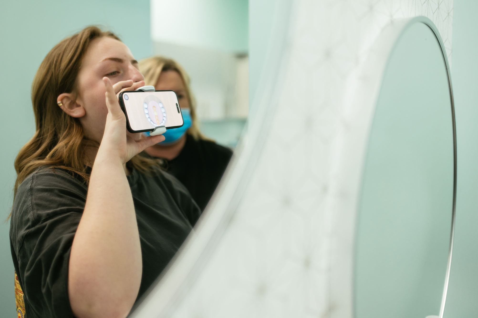 Patient using a phone with a ScanBox attachment to take a Dental Monitoring scan of her teeth