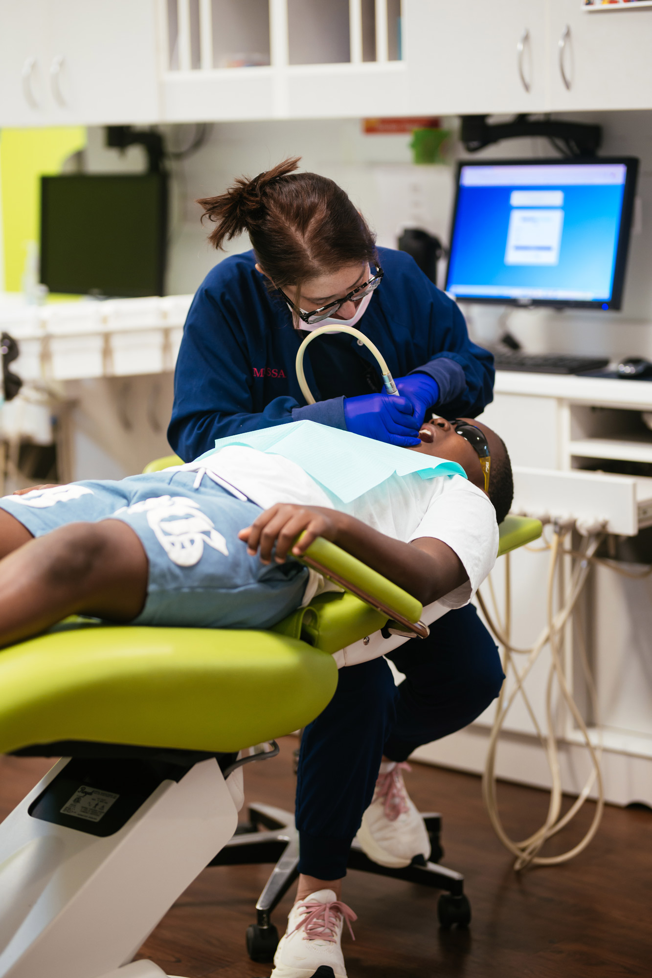 Pediatric dental hygienist performing a gentle teeth cleaning on a child wearing protective glasses at the Short Pump office