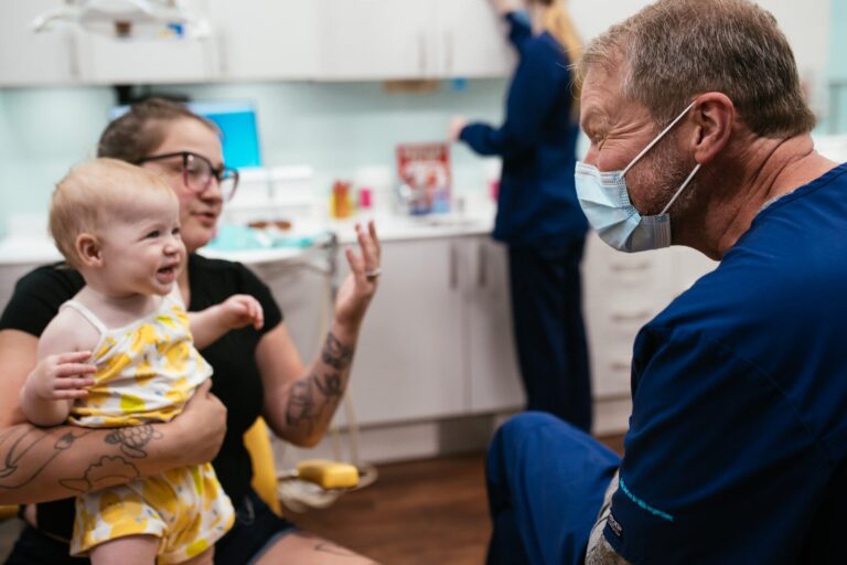 A smiling baby on a parent's lap during a first dental visit at RPDO